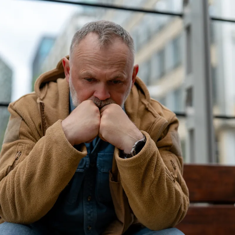 ketamine and alcohol. A man sitting on wooden bench looking down with his hands on his chin.