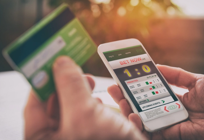 Why Gambling is Addictive. An image of a person holding their debit card whilst accessing a gambling betting website on their phone.