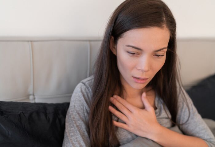 Difficulty Breathing After Drinking Alcohol. An image of a woman holding her chest, indicating she is experiencing shortness of breath.