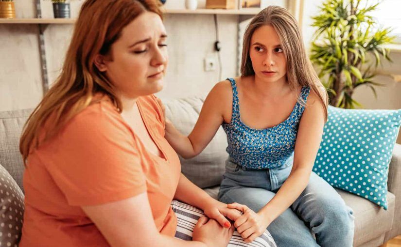 Two women sat on sofa, holding hands in comfort