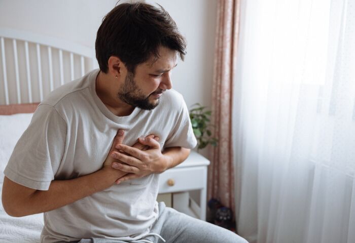What Causes Heart Pain After Drinking Alcohol - an image of a man sat at the edge of his bed holding his chest, indicating he is experiencing chest pain