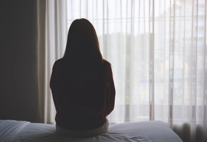 The Link Between Cocaine and Depression. An image of a woman sitting alone on a bed in bedroom.