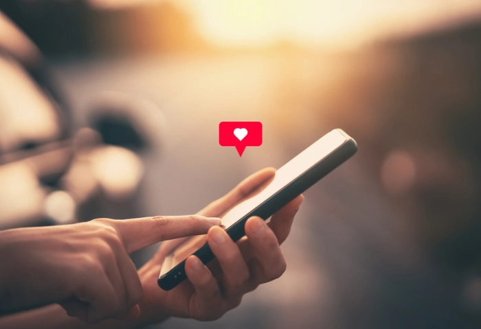 Are dating apps addictive? An image of a woman's hand holding and using her using smart phone with an illustration of a heart icon at outdoor park street background